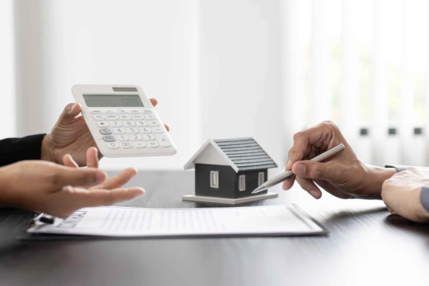 Taxa de juros do Minha Casa Minha Vida em negociação: mãos calculando com calculadora e assinando documentos sobre uma maquete de casa em mesa, simbolizando análise de financiamento habitacional.